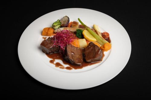 a white plate of food with meat and vegetables at Hotel Crusch Alba Zernez in Zernez