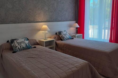 two beds in a hotel room with red curtains at appartement 4 pers dans longère à 800m de la plage in Plouhinec