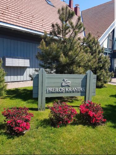 a sign in the grass with flowers in front of a building at Cozy modern apartment with lagoon view in Preila