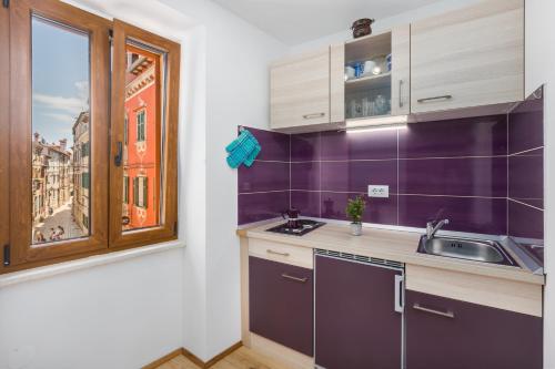 kuchnia z fioletowymi ścianami, umywalką i oknem w obiekcie Apartment Lanterna Veneziana w Rovinj