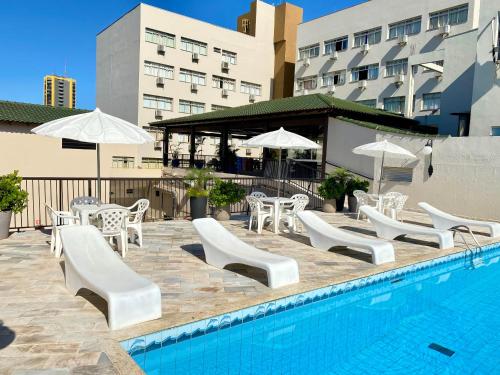 a pool with white chairs and tables and umbrellas at San Rafael Comfort Class Hotel in Foz do Iguaçu