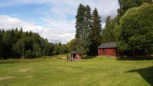 a red barn in a grassy field next to a tree at Geijersholms Herrgård in Hagfors