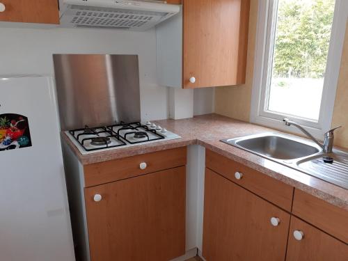 Il comprend une cuisine équipée d'une cuisinière. four supérieur à côté d'un évier dans l'établissement mobil-home sur terrain privatif jean-mi et flo, à Vendays-Montalivet