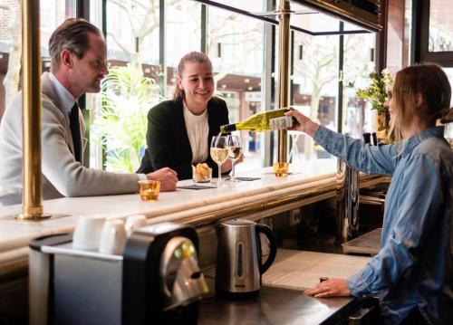 une femme versant un verre de vin dans un bar dans l'établissement Hotel Lundia, à Lund