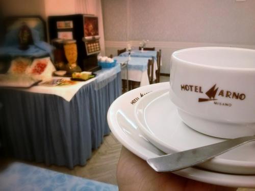 a person holding a coffee cup on a plate at Hotel Arno in Misano Adriatico