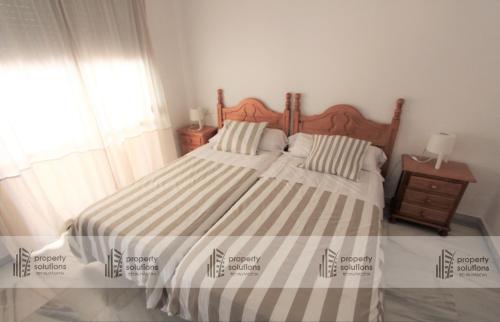 1 dormitorio con 1 cama grande con colcha a rayas en Pueblo Del Parque 3 - Terraza soleada con jardín - Piscina y Playa - Urbanización tranquila, en Benalmádena
