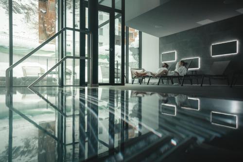 two women sitting on chairs in a room with a pool at Alpen Resort & Spa in Zermatt