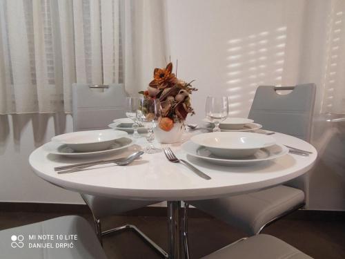 a white dining table with plates and glasses and a cat centerpiece at Apartments Drpic in Gabonjin