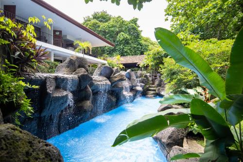 a waterfall in front of a house with rocks at Pumilio Mountain & Ocean Hotel in Jacó