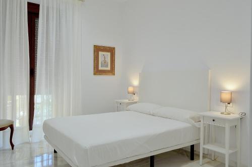 a white bedroom with a bed and two tables at SunShine Cruz Conde in Córdoba