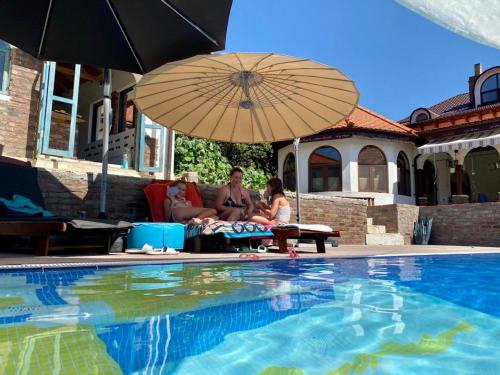 two people sitting under an umbrella next to a swimming pool at Conacul Grigorescu in Răteşti