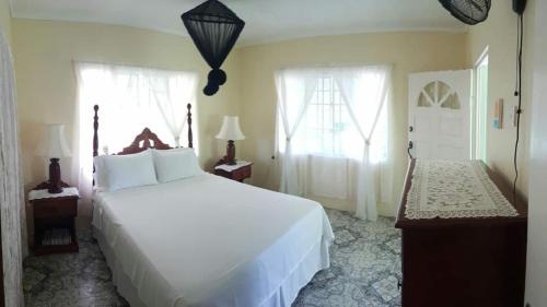 a bedroom with a large white bed and two windows at Rock Side Villa On the Beach in Treasure Beach