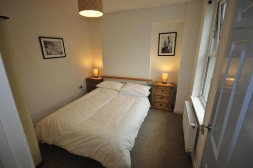 um quarto com uma cama com lençóis brancos e 2 candeeiros em Surf View Apartment, Newquay em Newquay