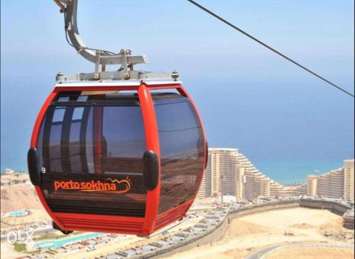 a red cable car in front of a city at Porto sokhna Pyramids family only in Al Ḩafāʼir