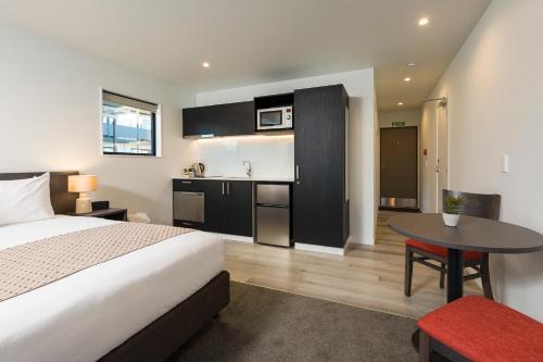 a bedroom with a bed and a table and a kitchen at Carnmore Hagley Park in Christchurch