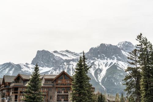 a building with trees and mountains in the background at Spring Creek Spacious Luxury King One Bedroom plus Den at White Spruce Lodge in Canmore