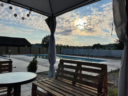 a wooden bench sitting under an umbrella near a pool at Holiday Home Rodjak sa sela in Mionica