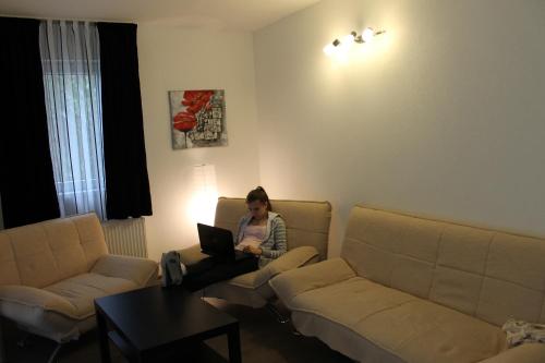 a woman sitting on a couch with a laptop in a living room at Pensiunea Alpina in Malaia