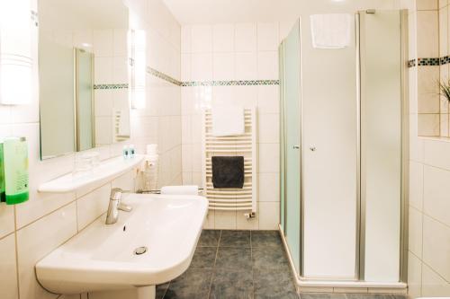 a white bathroom with a sink and a shower at Hotel Schiffer in Bensersiel