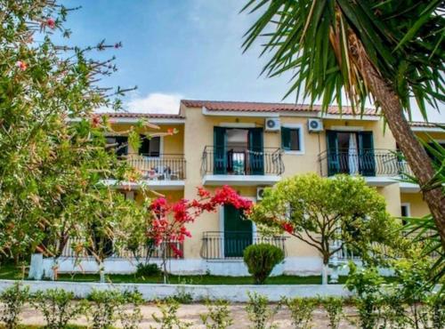 Casa amarilla grande con balcón y árboles en Lemon Tree Apartments B C, en Argostoli