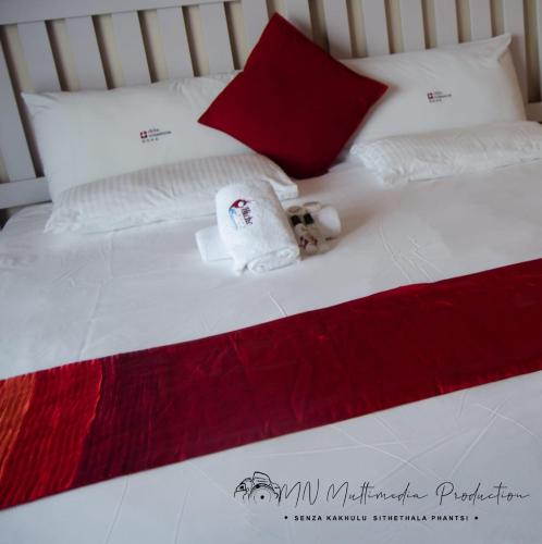 a white bed with red and white pillows and a towel at Smart Diva Accommodation in East London