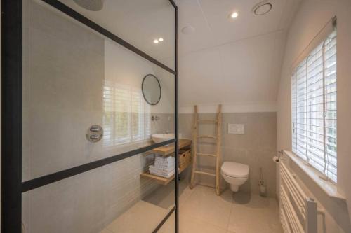 a bathroom with a toilet and a glass shower door at Sous les Dunes in Schoorl
