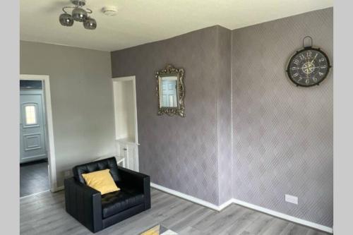 a room with a chair and a clock on a wall at Beautiful two bedroom flat by the Loch in Balloch