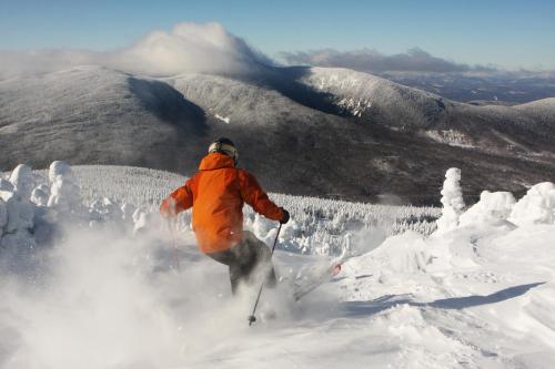 a person in an orange jacket skiing down a snow covered slope at Sugarloaf Mountain Hotel in Carrabassett