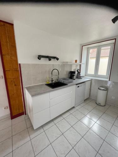 a white kitchen with a sink and a window at Le petit écrin champenois in Étoges