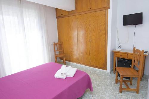 1 dormitorio con cama morada, escritorio y silla en Pensión Felipe, en Carboneras