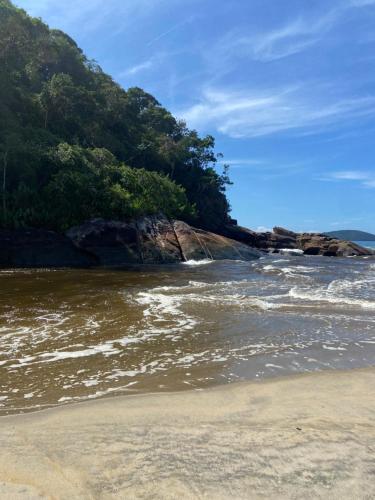 a beach with the ocean and trees in the background at Casa da Si Hostel in Ubatuba