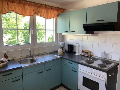 eine Küche mit blauen Schränken, einem Waschbecken und 2 Fenstern in der Unterkunft Wiesenblick in Grube