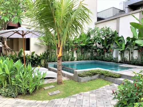a swimming pool in a garden with a palm tree at Dee Mansion in Denpasar