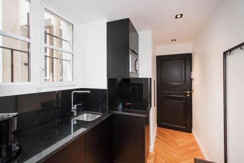 d'une cuisine avec des comptoirs noirs, un évier et une fenêtre. dans l'établissement Odéon - Notre Dame Paris Climatisé-Wifi, à Paris