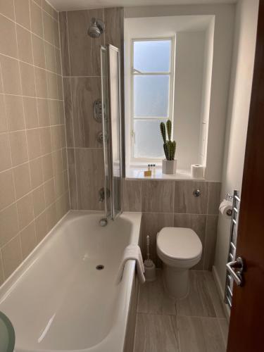 a bathroom with a tub and a toilet and a window at Roland House in London