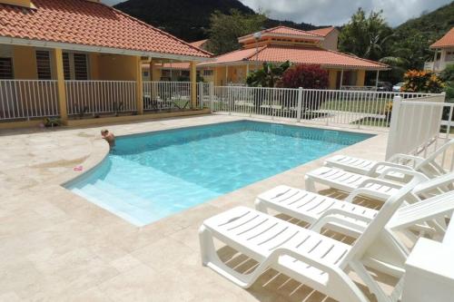 a swimming pool with white chairs and a house at Séjour de rêve en Martinique 6 pers avec piscine in Les Trois-Îlets