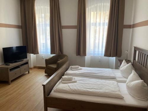 a bedroom with two beds and a chair and a television at An der Porzellan-Manufaktur Pension in Meißen