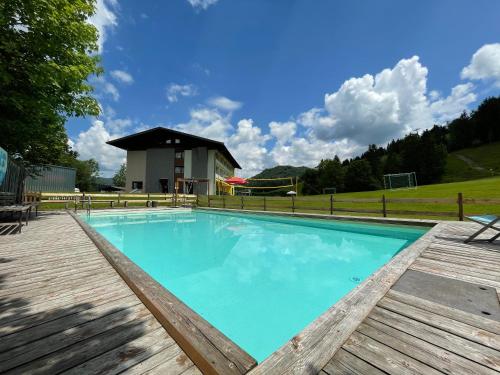 a swimming pool with a wooden deck and a house at Sportgästehaus Unterberg in Kössen