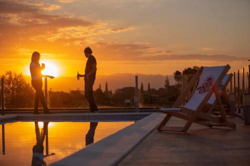 a couple standing on the edge of a pool with the sunset at ÑU Posta Urbana Hotel Boutique in Córdoba
