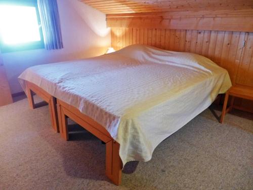 a bed in a bedroom with a wooden wall at Apartment Arsets 203-12 by Interhome in Arveyes