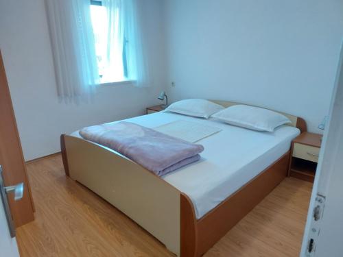 a bedroom with a bed with white sheets and a window at Apartmani Jašarević in Martinšćica