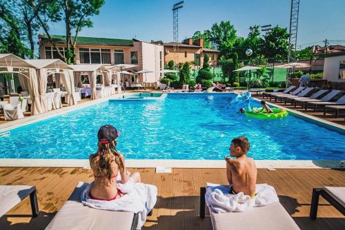 two people sitting on chairs in front of a swimming pool at Arcadia Plaza Hotel in Odesa