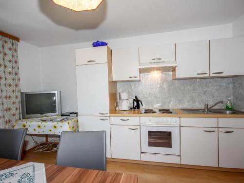 a kitchen with white cabinets and a sink and a tv at Apartment Jägerhof-1 by Interhome in Hochpillberg