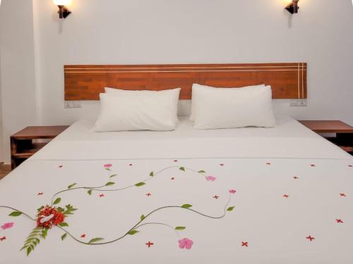 a bed with a white bedspread with flowers on it at Dhonkamana Stay in Thoddoo