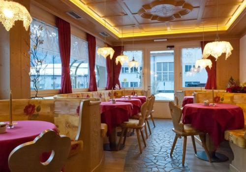a restaurant with red tables and chairs and windows at Hotel Bellaria in Predazzo