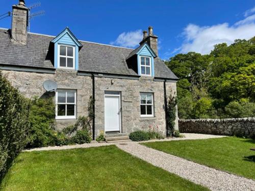 a large stone house with a grass yard at Burnside Cottage on the Blarich Estate in Rogart