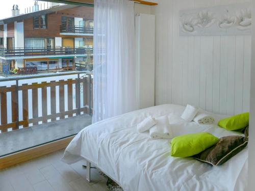 a white bed with green pillows in a room with a balcony at Studio Grenier 5 by Interhome in Nendaz