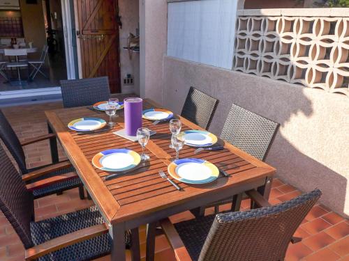 einen Holztisch mit Tellern und Weingläsern auf einer Terrasse in der Unterkunft Holiday Home Hameau des Tamarins-1 by Interhome in Le Barcarès