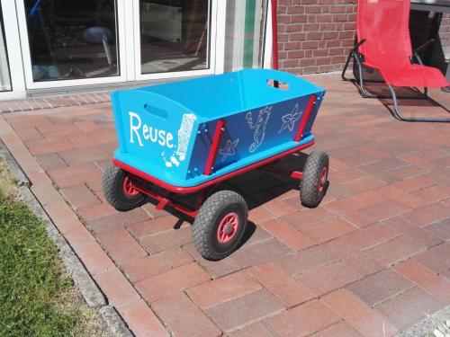 a blue wagon with wheels sitting on a brick sidewalk at Holiday Home Reuse by Interhome in Norddeich