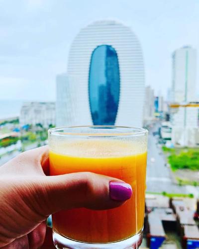 a hand holding a glass of orange juice in front of a city at Orbi city in Batumi